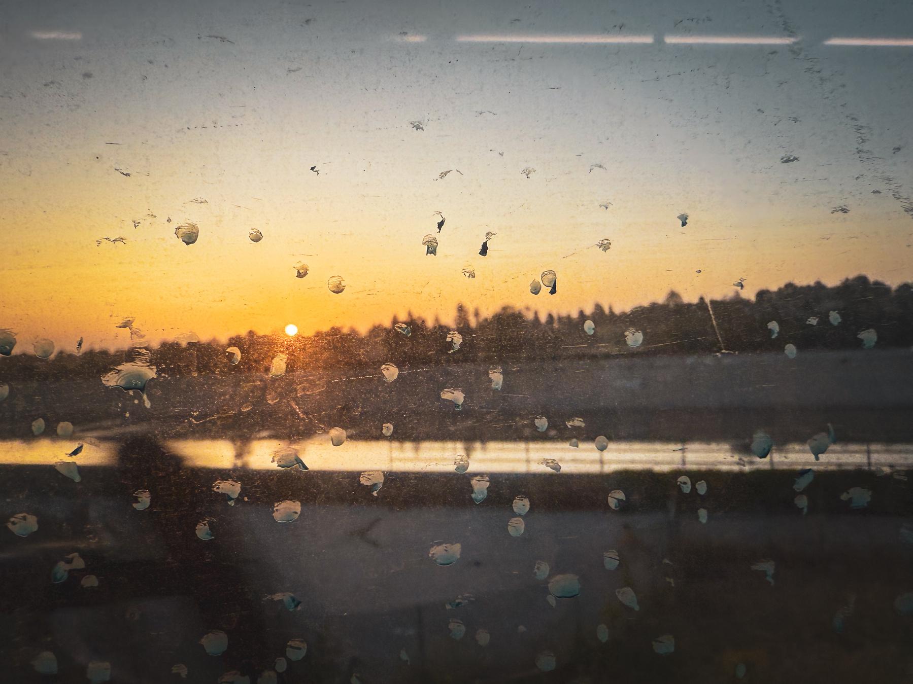 A scenic sunrise view is visible through a dirty window with smudges and blurred reflections of a landscape.
