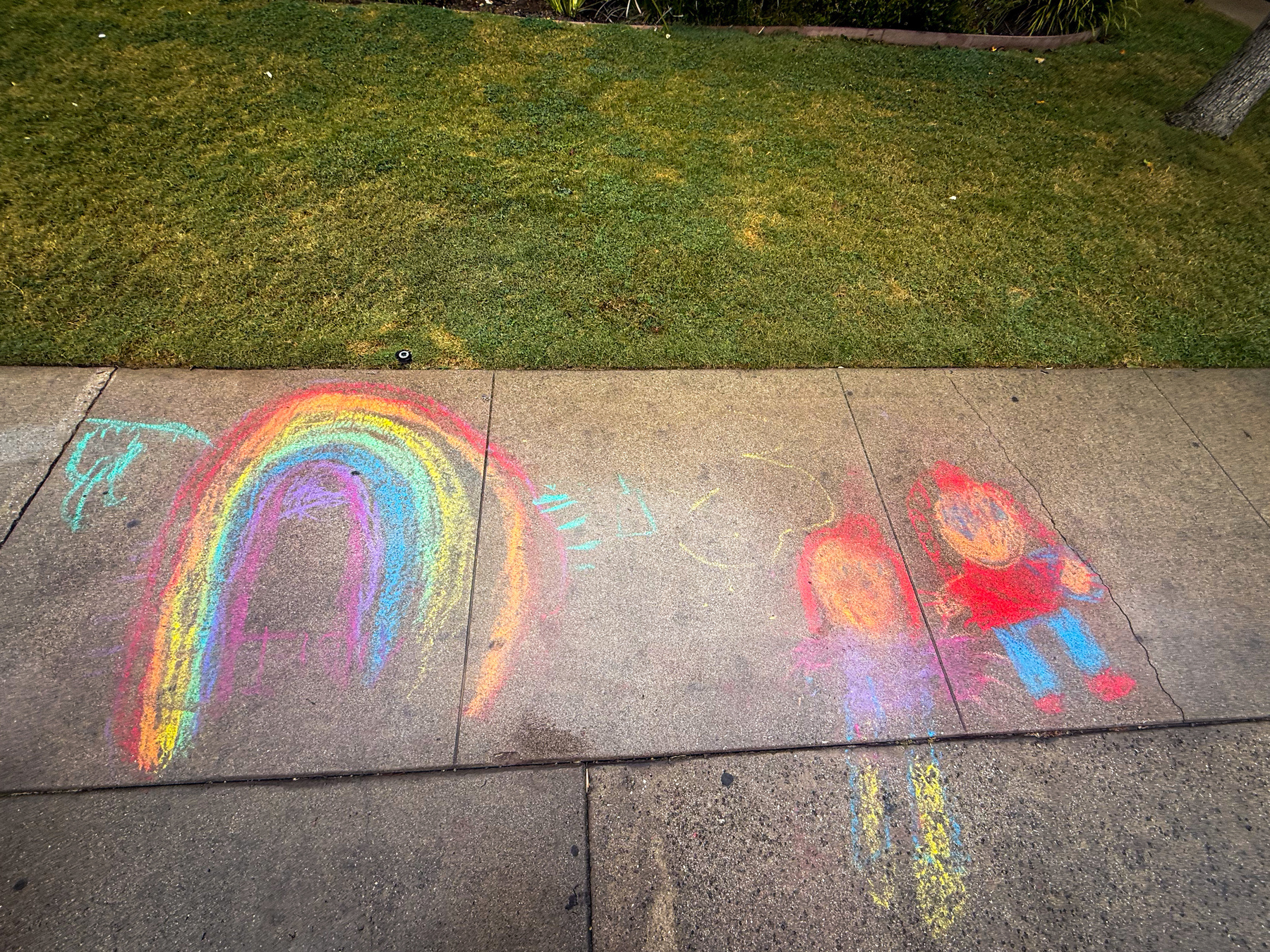 Colorful chalk drawings on a sidewalk depict a rainbow and two human figures.