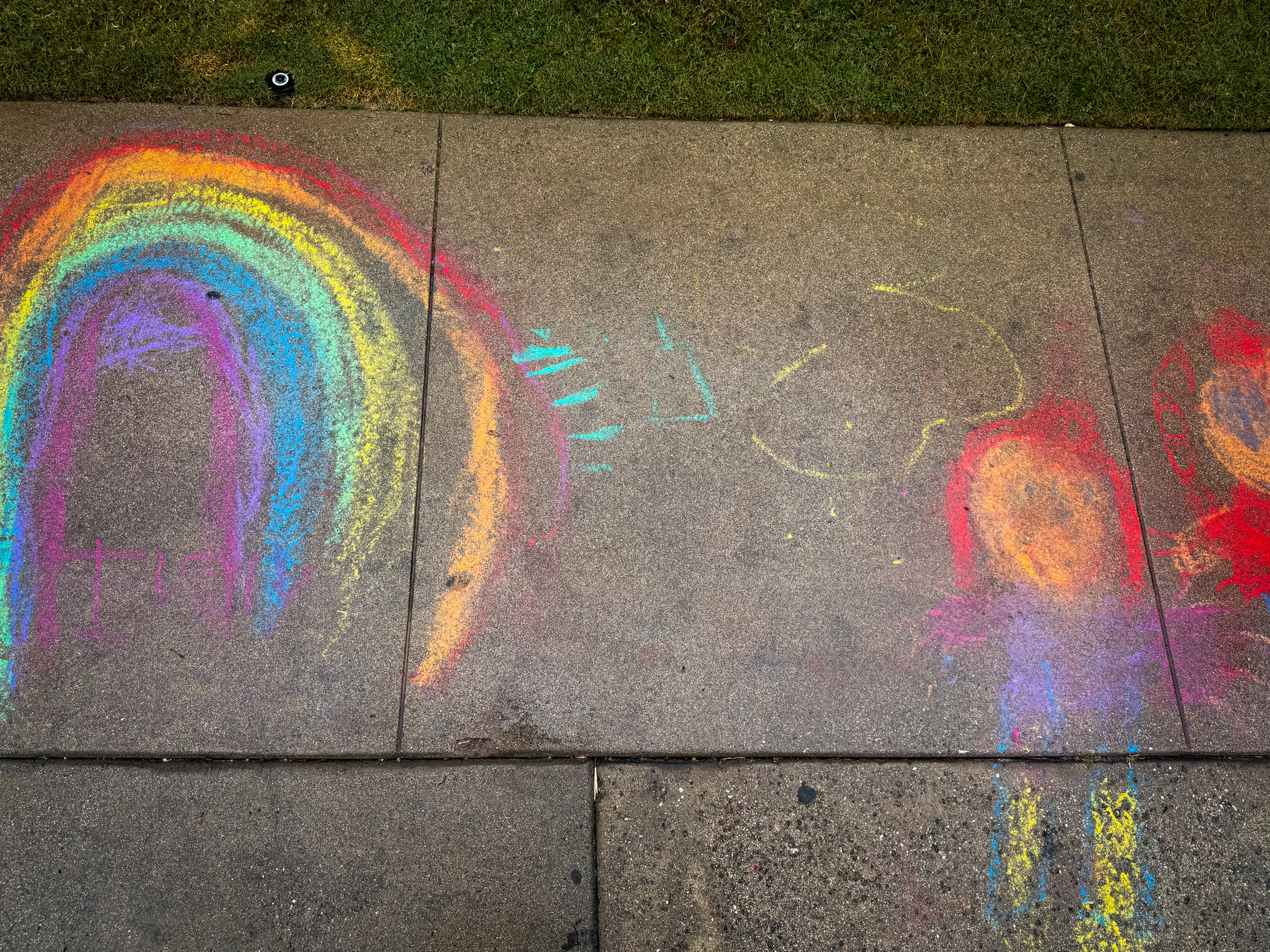 Colorful chalk drawings, including a rainbow and other shapes, adorn the concrete sidewalk.